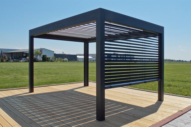 Pergola moderne noire sur terrasse en bois clair, avec store à lames orientables fermé sur un côté, offrant ombre et style.