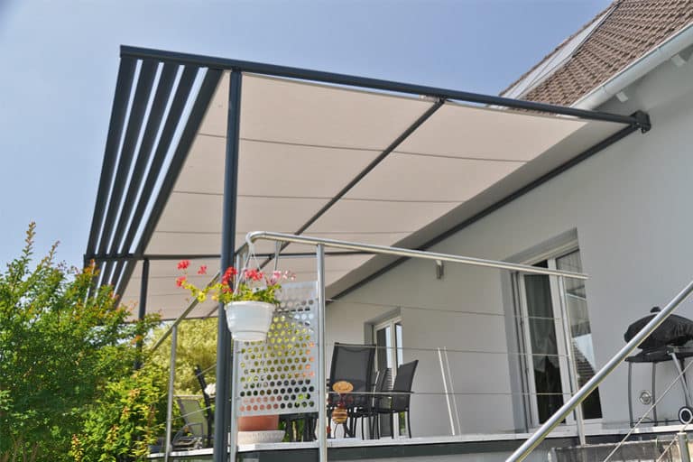 Pergola moderne avec toit rétractable en tissu beige et structure noire, offrant de l'ombre sur une terrasse avec garde-corps en inox et plantes fleuries.