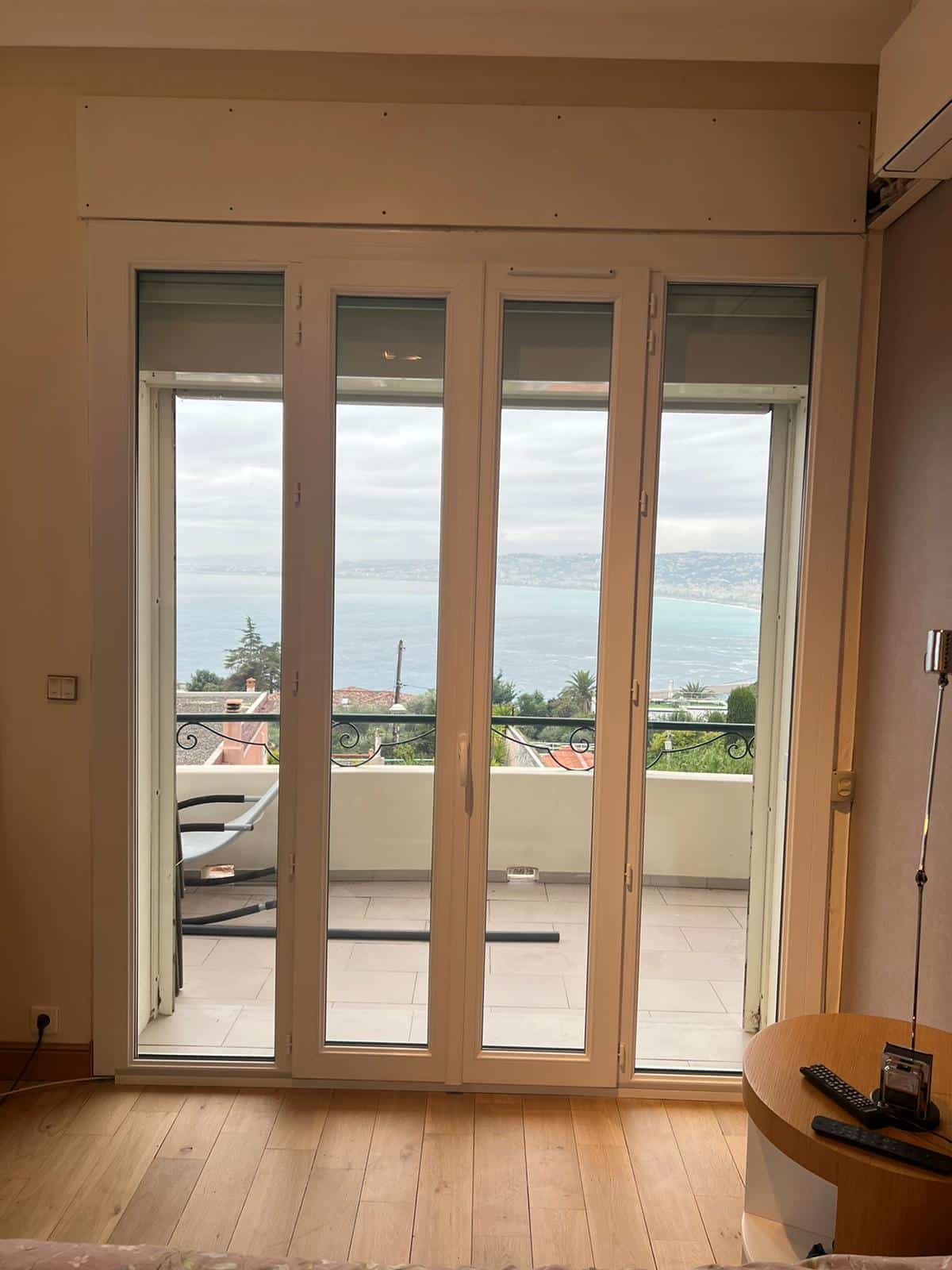 Intérieur moderne avec plancher bois, ouvrant sur une terrasse via une baie vitrée accordéon. Superbe vue sur la mer Méditerranée et la côte.