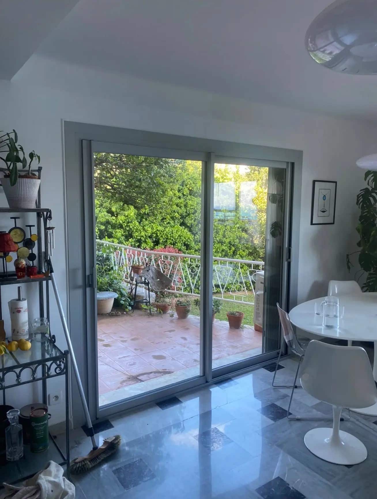 Salle à manger lumineuse avec porte vitrée coulissante menant au jardin. Sol en marbre brillant, table design et verdure luxuriante.